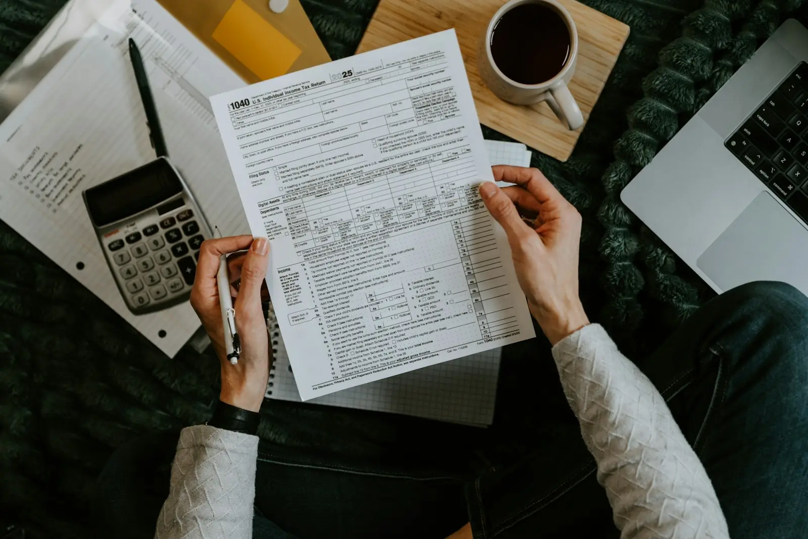 Hands holding forms beside a calculator and laptop